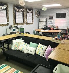 a couch with many pillows on it in a room filled with desks and chairs