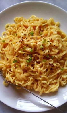 a white plate topped with pasta and parsley on top of a table next to a fork