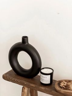 a black vase sitting on top of a wooden table next to a candle and bowl