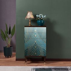 a blue and gold cabinet next to a potted plant on top of a wooden floor