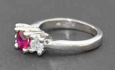 This is a very fine grade Ruby Ring. It is crafted from solid thick Platinum. The ring hold three stones. The center being a very fine grade natural untreated Ruby. It is a round cut and set very securely with four raised prongs. The ruby is of fabulous quality no visible inclusions or abrasions. The color is a deep red with a pink hue. The first two photographs are in natural morning light. The fine stone changes color under different light as you can see from the photographs. On either side of Luxury Ruby Three Stone Rings, Classic Three Stone Ruby Ring With Diamonds, Formal Solitaire Ruby Ring With Round Cut, Classic Ruby Ring With Vvs Clarity, Classic White Gold Ruby Ring With Round Stone, Formal Three Stone Emerald Cut Birthstone Ring, Ruby Ring With Accent Stones In Platinum, Formal Three-stone Emerald-cut Birthstone Ring, Emerald Cut Three Stone Birthstone Ring For Formal Occasions