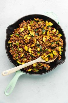 a skillet filled with meat and vegetables on top of a white table next to a wooden spoon