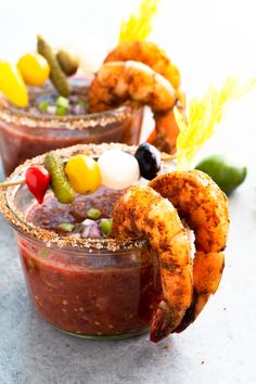 two glasses filled with food and garnishes on top of a white table