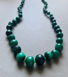 This beaded necklace features large natural malachite beads and small glass beads. Malachite Gemstone Bead Necklaces, Malachite Gemstone Beads Necklace, Polished Malachite Round Beaded Necklaces, Round Malachite Beaded Necklace, Green Oval Beads Necklace With Spiritual Style, Green Oval Beads Necklace In Spiritual Style, Green Oval Beads Spiritual Necklace, Spiritual Green Necklace With Oval Beads, Beaded Green Onyx Round Beads Necklace