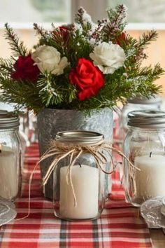 a table topped with mason jars filled with white and red flowers on top of a checkered table cloth