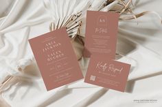 wedding stationery on top of a bed with white sheets and pink flowers in the background