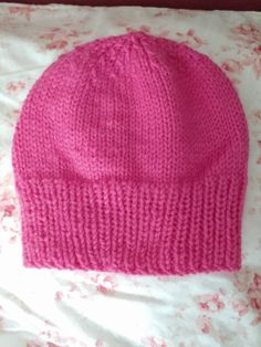 a pink knitted hat laying on top of a bed