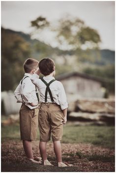 two young boys standing next to each other in shorts and suspenders looking at something