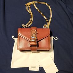 *Moving Sale* My Authentic Chlo Aby Chain Mini Shoulder Bag Needs A New Home! Brown Leather + Gold Chain. Excellent Condition! 0 Scratches / Marks. Comes With Dust Bag, Authenticity Card, Removable Gold + Leather Lock With Key, And Semi-Adjustable Gold Chain Strap (I Cannot Remove It). There Is 1 - Card Slot On The Envelope Side. This Bag Can Be Used 2 Ways: 1) Cross-Body 2) Shoulder Bag It's A Gorgeous Piece That I Purchased From Bloomingdale's In 2020. Gorgeous Bag, But I Need To Make Room Bec Luxury Chain Bags As Gift, Luxury Chain Bag As Gift, Brown Bag With Lock For Evening, Designer Shoulder Bag With Chain Strap As Gift, Leather Shoulder Bag With Chain Strap As Gift, Cognac Bag With Chain Strap For Everyday Use, Elegant Cognac Shoulder Bag With Chain Strap, Luxury Shoulder Bag With Chain As Gift, Elegant Cognac Bag With Chain Strap