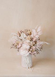 a white vase filled with lots of flowers on top of a table next to a wall