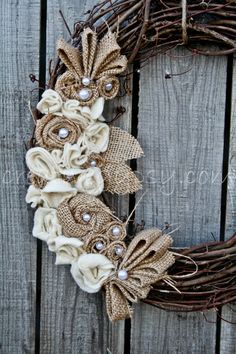 a wreath made out of burlock and fabric flowers on a wooden fence with pearls