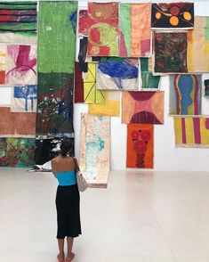 a woman standing in front of a wall covered with paintings and art hanging from it's walls