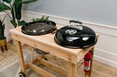 two bbq grills sitting on top of a wooden table next to a potted plant