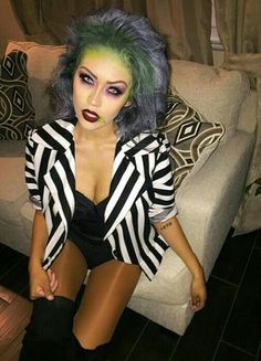 a woman with green hair and makeup sitting on a couch next to a white couch