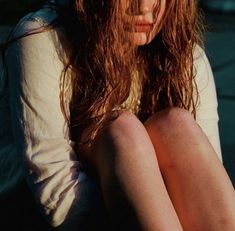 a young woman sitting on the ground with her hands behind her head and looking down