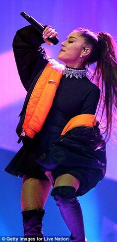 the singer is performing on stage with an orange vest over her shoulders and black boots