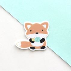 a small sticker with a fox holding a pacifier in its mouth on a blue and white background