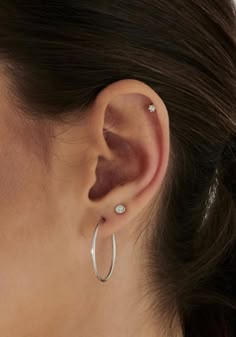 a woman wearing a pair of silver hoop earrings with white stones on the side of her ear