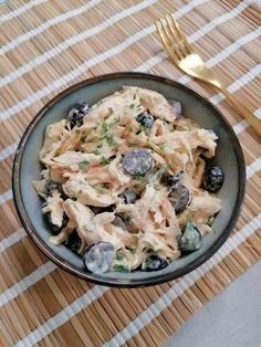 a bowl filled with pasta and blueberries on top of a place mat next to a fork