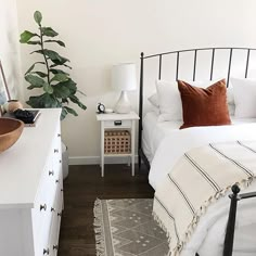 a bedroom with a bed, nightstands and a plant on the side table in front of it