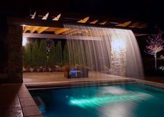 a pool at night with lights on and water running from the top to the bottom