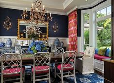 a formal dining room with blue and white walls, red upholstered chairs, chandelier, windows, and rugs