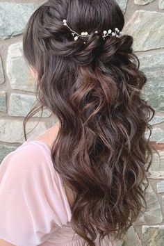 a woman with long hair wearing a flowered headpiece in front of a stone wall