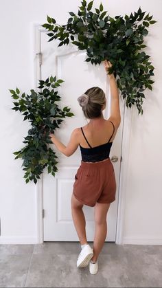 a woman is holding up some plants in front of a door and reaching for it