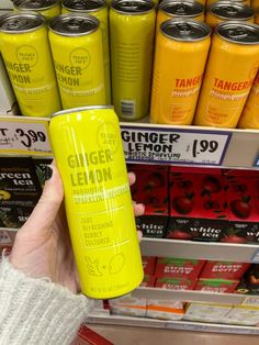 a person holding up a can of ginger lemonade in front of a store shelf