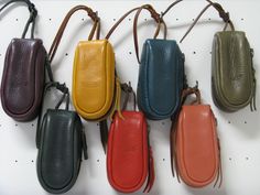 six different colored leather purses hanging on a white pegboard with string attached to them