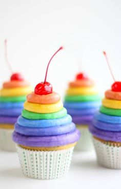 an image of some cupcakes with rainbow frosting and cherries on top