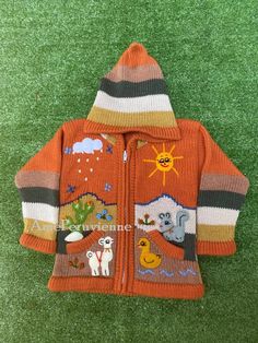 an orange jacket with animals on it sitting on the grass in front of green grass