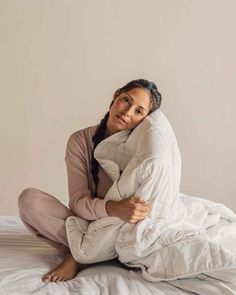 a woman sitting on top of a white bed covered in a comforter and pillows