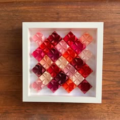 a white frame with red and pink squares in it on top of a wooden table