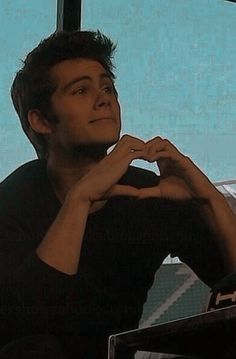 a man sitting in front of a window making a heart shape with his hands while looking up