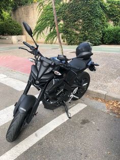 a black motorcycle parked on the street next to a tree and sidewalk with no traffic