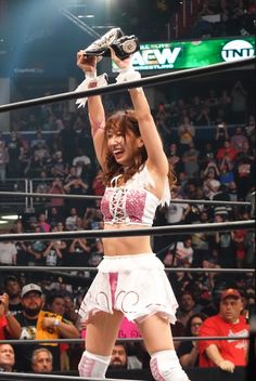 a woman in a white outfit holding up a trophy while standing on top of a wrestling ring