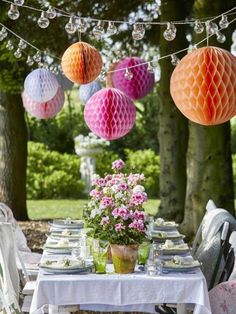 an outdoor table with paper lanterns hanging from the ceiling and flowers in vases on the table