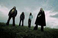 four people standing on top of a grass covered hill in front of clouds and sky