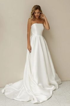 a woman wearing a white wedding dress standing in front of a wall with her hand on her head