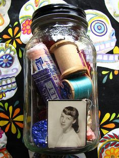 a jar filled with thread and spools on top of a table