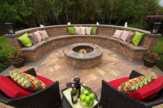 an outdoor fire pit surrounded by wicker chairs and red cushioned cushions with green apples on the table