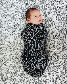 a baby wrapped in a black and white blanket laying on top of graffiti covered wall