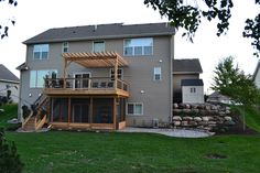 a large house with a deck in front of it and grass around the back yard