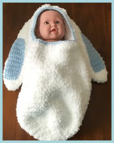 a baby doll laying on top of a wooden floor wearing a white and blue blanket