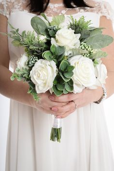 a bride holding a bouquet of white roses and greenery in her hands, on a white background