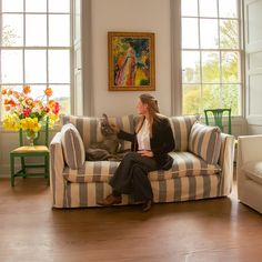 a woman sitting on top of a striped couch next to a dog in a living room