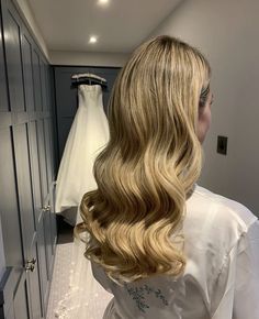 a woman with long blonde hair standing in front of a wedding dress on a hanger