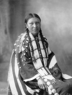 an old black and white photo of a native american woman sitting in front of a flag