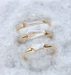 three gold rings with white stones on them sitting in the snow, one has an arrow shaped band